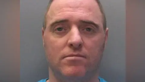 Northumbria Police Mugshot of McDonald starring glumly at the camera. He has brown and grey hair and stubble. 