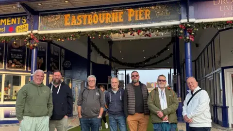 Seven men standing in front of Eastbourne Pier.