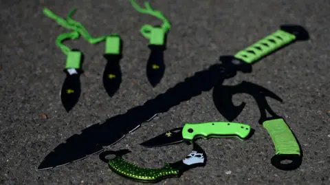 PA Media Some examples of 'zombie knives' at a secure police location. The knives have various sized blades and green handles, including a large knife with a serrated edge. 
