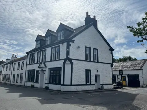 A white hotel building with black surrounds to the windows under a whispy-clouded sky