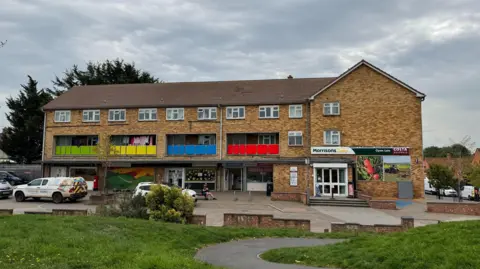 Shop and block of two-storey flats in Bridgwater. There's several shops and a few cars parked outside.