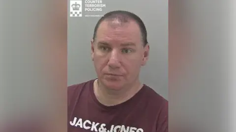 West Mercia Police A man with receding short dark hair is wearing a burgundy t-shirt with Jack&Jones written on the front in block white capital lettering. 