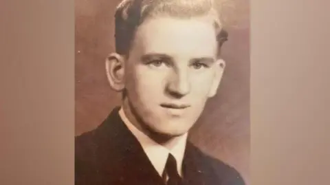 Bill Wake A black and white photograph of Bill Wake as a young man wearing a black suit and a black tie 