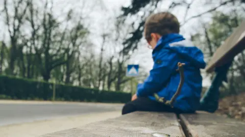 Little boy sat on alone on a bench.