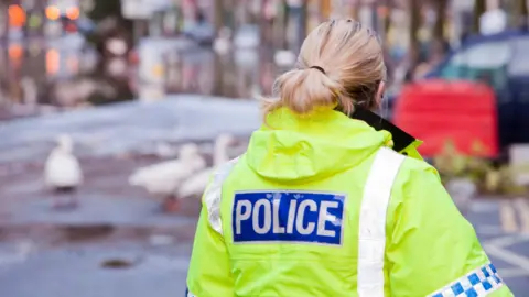 A police officer in a bright yellow jacket with police written on the back.