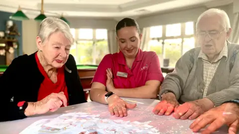 Mark Norman Care home residents and a member of staff sit at a table interacting with  with projected lights on the table.