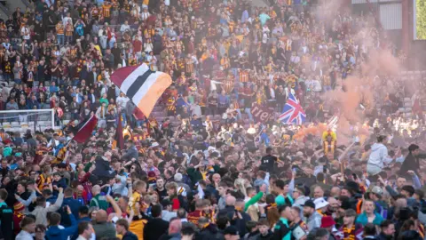 PA Media Bradford City fans celebrate promotion in stands and on the pitch at the University of Bradford Stadium, with many waving flags and letting off flares.