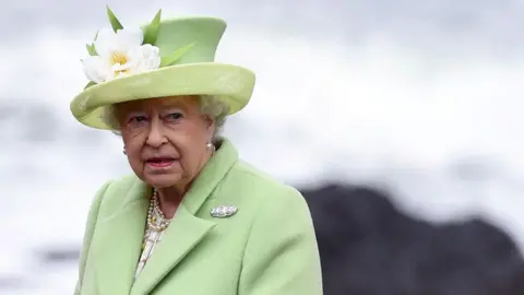 Reuters Ratu Elizabeth II mengenakan topi berhiaskan bunga putih dan mantel berwarna hijau pucat saat berkunjung ke Irlandia Utara. 