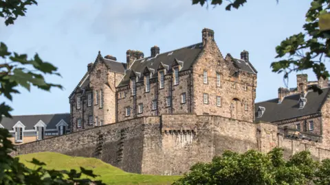 Getty Images A grand castle, surrounded by a high wall. It is positioned on a hill.