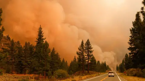 Getty Images A car driving down a road towards huge clouds of smoke as fires burned in Markleeville, California