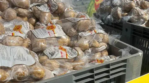 Piles of potatoes in clear plastic bags sit in a large grey container.