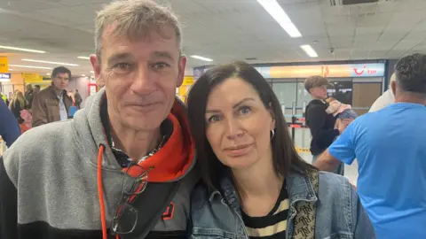 A man wearing a hoodie standing next to a woman with black hair wearing a denim jacket and a striped top