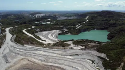 Aerial shot of clay mining area in Cornwall. It shows dirt roads and a pit full of turquoise blue water.
