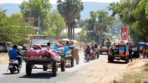 Reuters Villagers in the Oddar Meanchey Province, Cambodia fleeing with their belongings on tractors, bikes and vans. We see them from behind as they drive away
