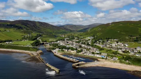 Getty Images An aerial view of the village of Helmsdale on the east Sutherland coast. The village has a culster of houses and other buildings on a hillside, and there is a historic harbour. Green hills rise behind the village. It is pictured on a sunny day with white, fluffy clouds in the sky.