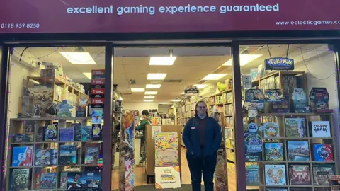 A woman wearing dark trousers and a coat standing in the doorway of a board games shop.