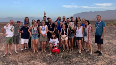 Supplied Coleen Coxon is kneeling at the front of the group of walkers holding her medal