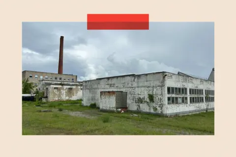 An abandoned concrete building with a cooling tower in the background