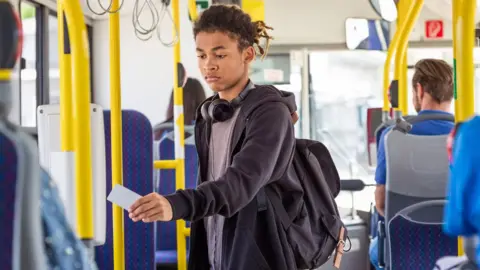 Getty Images Teenage boy walks down bus holding a contactless payment card