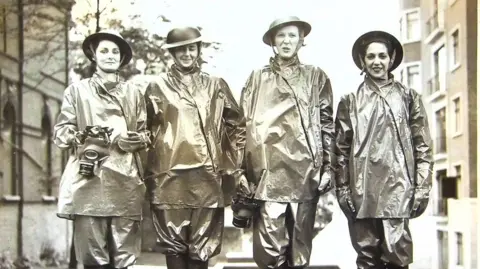 London Ambulance Service Four women standing, looking at the camera, wearing gas protection suits which appear as though made of tin foil