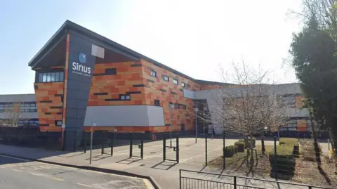 Google Street View picture of Sirius Academy North. The school has colourful brickwork on its side with a black pillar saying "Sirius Academy North" on its sign.