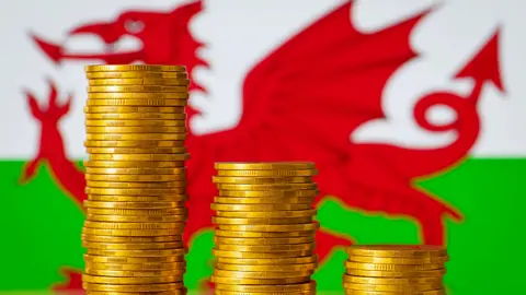 Three piles of coins in reducing stacks with a Welsh flag in the background