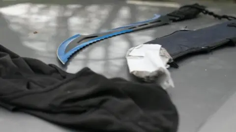 A large curved zombie knife with a bright blue edge lies on the roof of a car pulled over by police