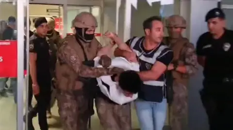 A still of the suspect in a stabbing in Eskisehir, Turkey being escorted from a hospital to a vehicle by police.