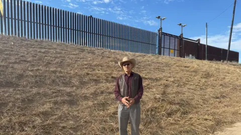 Bernd Debusmann Jr/BBC News Demesio Guerrero stands next to the border wall in Hidalgo, Texas. 