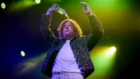 Getty Images Matt Bowman of The Pigeon Detectives performs onstage during the Isle of Wight Festival at Seaclose Park on June 19, 2025 in Newport, Isle of Wight. He can be seen pouring a bottle of water over his long curly hair.