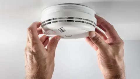 Getty Images hands adjusting a smoke alarm on a ceiling