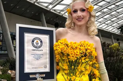 Arthur Williams Marmalade wearing a yellow dress covered in daffodils. She is holding a Guinness World Records certificate. 