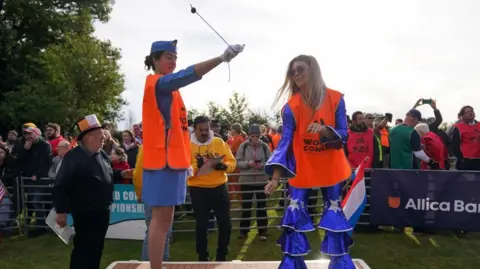 PA Media Two female competitors, both in blue fancy dress outfits, on a platform taking part in the competition while being watched by judges and spectators