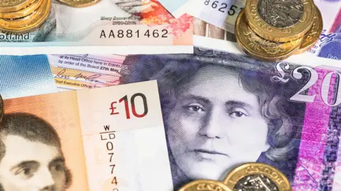 £5, £10 and £20 notes scattered on a surface with piles of £1 coins on top