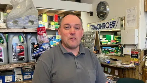 Grace Wood/BBC A man with short brown hair wearing a grey polo shirt stands in a hardware store