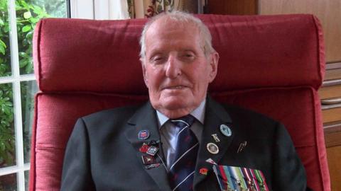 98-year-old Norman Bartlett in a shirt, tie and jacket with medals on the outside pocket