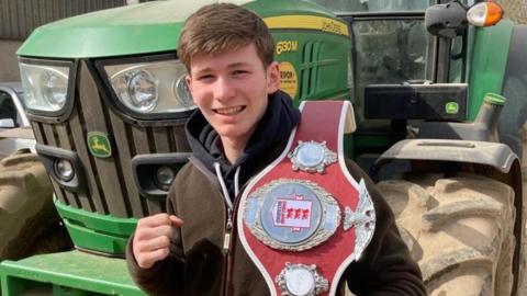 Edward posing with one of his belts in front of a tractor