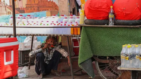 Getty Images A man eats ice-cream while taking shelter under a roadside stall on a hot summer day in Varanasi on April 23, 2026