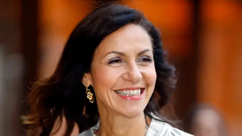 Julia Bradbury is in the middle of the image looking to the right of the image. She has shoulder length brown hair and brown eyes. 