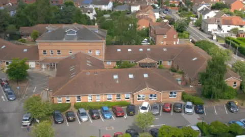 EPUT A photo of the King's Wood Centre in Colchester, which is a mental health treatment centre. The picture has been taken by a drone. It shows the large, sprawling brown building with a car park in front of it.
