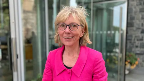 Deputy Yvonne Burford, who has short blonde hair, blue rimmed glasses and is wearing a pink jacket.