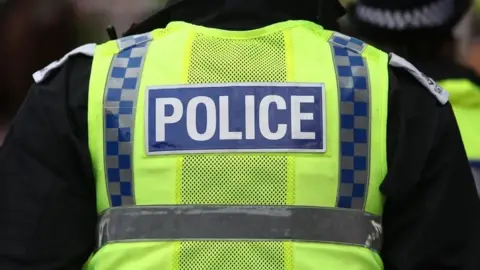 The back of police high-visibility neon yellow jacket, which has the word "POLICE" written on the back. 