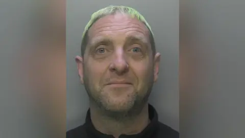 Surrey Police A mugshot of a man with short white hair.