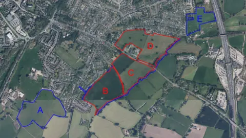Pegasus Group An aerial view of a map, showing fields marked in a blue and red, with housing seen to the top and left, and the M6 motorway to the right