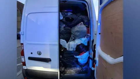 Hertfordshire police The rear of a white van parked on a street with its back doors open. The van's cargo area is completely packed with large plastic bags, leaving almost no visible empty space inside.
