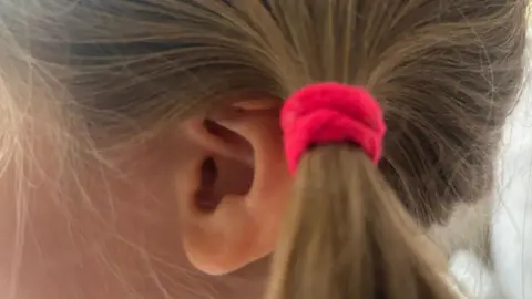 A child's ear - with a pink bobble in a blonde haired girl's bunches