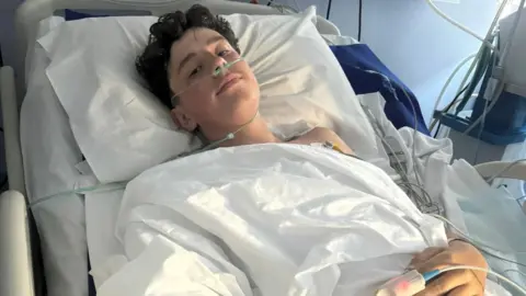 Family handout Alfie lies in a hospital bed with tubes connected to his nostrils and another medical device attached to a finger on his left hand