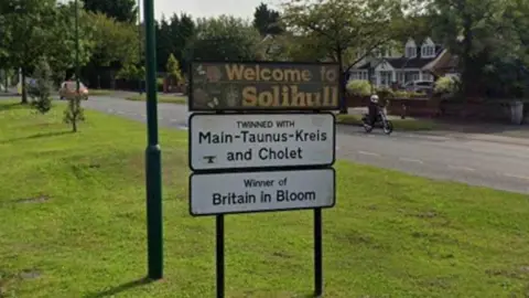 Google A "Welcome to Solihull" sign on a grass verge next to a lamp-post. Beneath the main sign is one saying "Twinned with Main-Taunus-Kreis and Cholet" and another saying "Winner of Britain in Bloom".