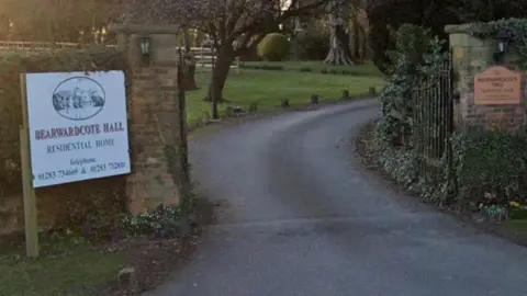 Sign which reads Bearwardcote Hall Residential Home to the left of a gate, with a road leading beyond the gates