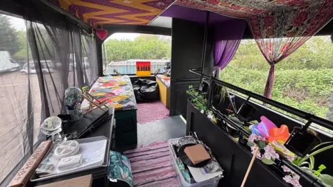 An interior view of the double decker bus' top deck. It has colourful furniture and decorations.